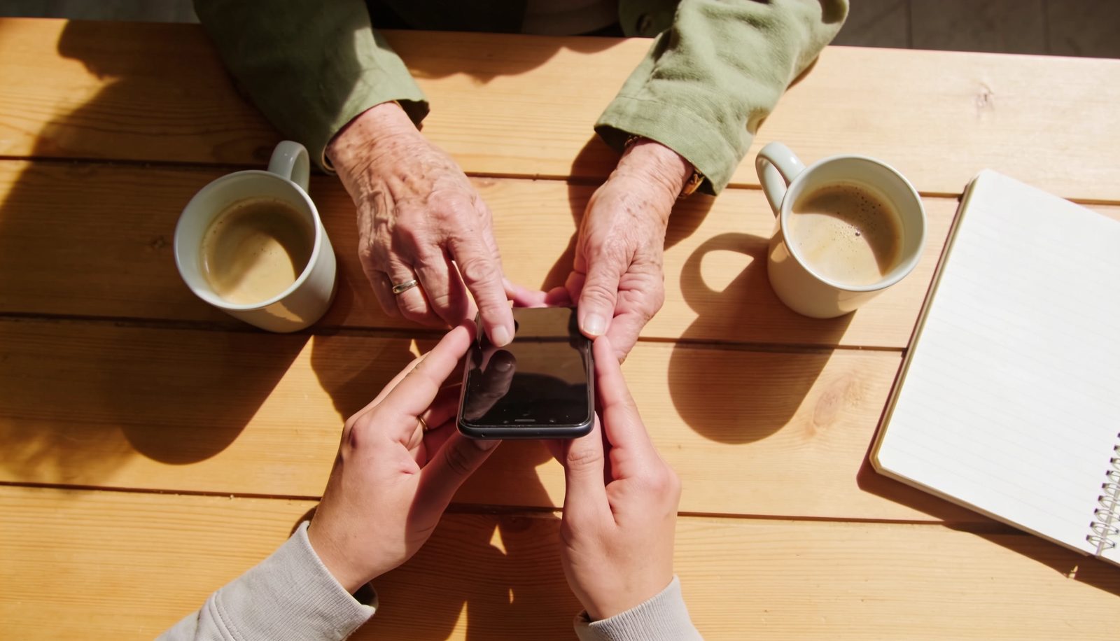 Manos de dos generaciones alrededor de un teléfono móvil sobre una mesa de madera